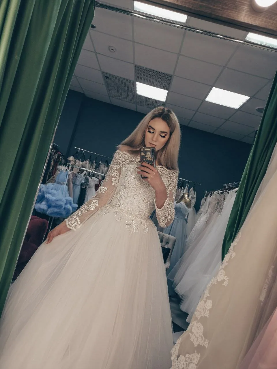 Невеста в кружевном платье фотографируется в зеркале салона